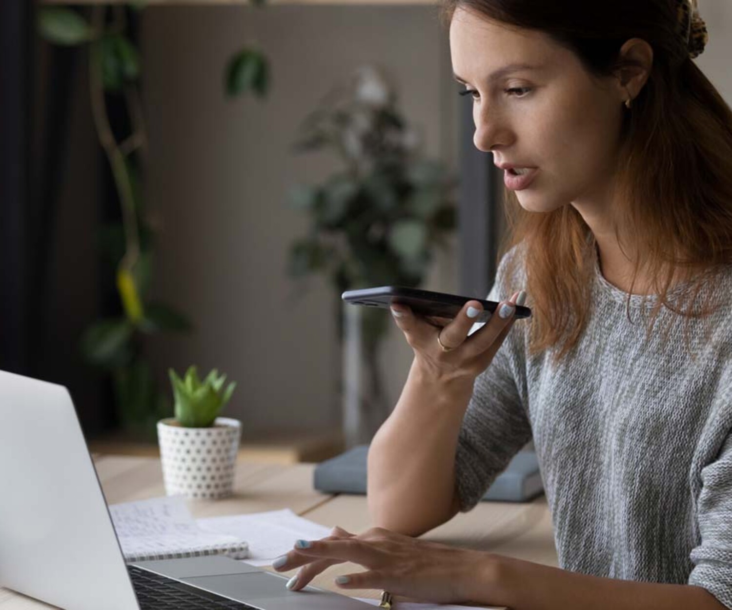Young woman recording into phone while working on laptop
