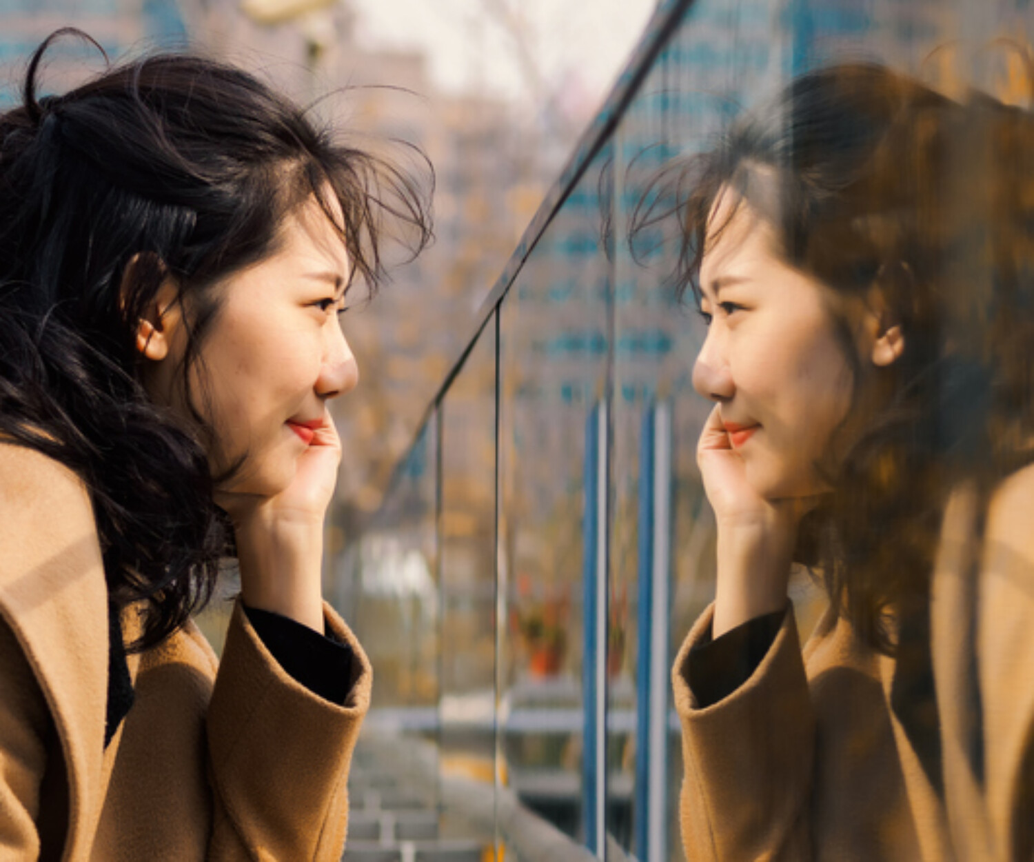 Beautiful Chinese girl looking at her mirror image in glass. Mirror and shadow reference for accent reduction.